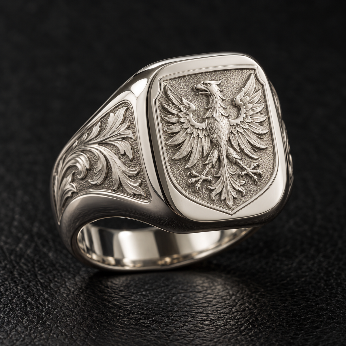 Ejemplo ilustrativo de anillo heráldico personalizado en oro blanco, con escudo de águila en relieve y grabados laterales sobre cuero negro